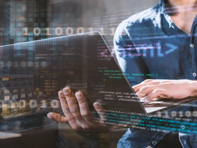 Homem de camisa azul trabalhando em notebook com sobreposição de código e números binários, ilustrando o conceito de product discovery aplicado ao desenvolvimento de software.
