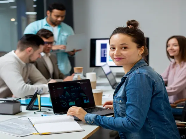 Equipe de desenvolvedores em escritório enquanto uma programadora olha para a câmera