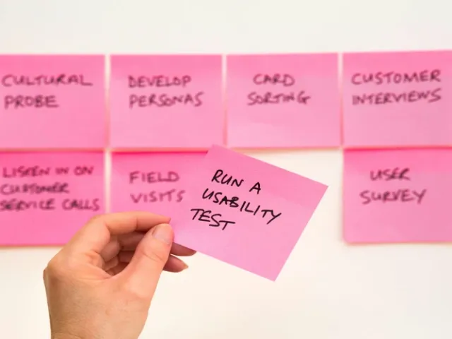 Post-its rosa colados em mural com uma mão segurando um deles escrito 'Execute o teste de usabilidade', ilustrando o método de validação com usuários