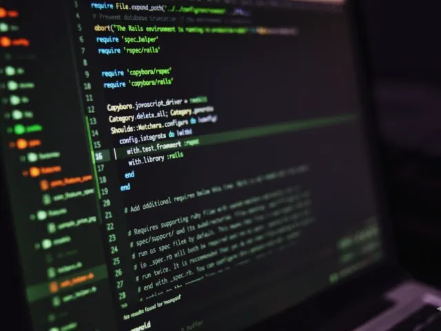 Tela de um laptop exibindo código-fonte em um ambiente de desenvolvimento, com linhas de código em tons verdes e roxos escuros, ilustrando a parte técnica do desenvolvimento de software.
