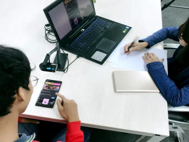 Dois profissionais de TI realizando teste de usabilidade de software em escritório com mesa branca, com celular e notebook sendo manipulados durante a sessão